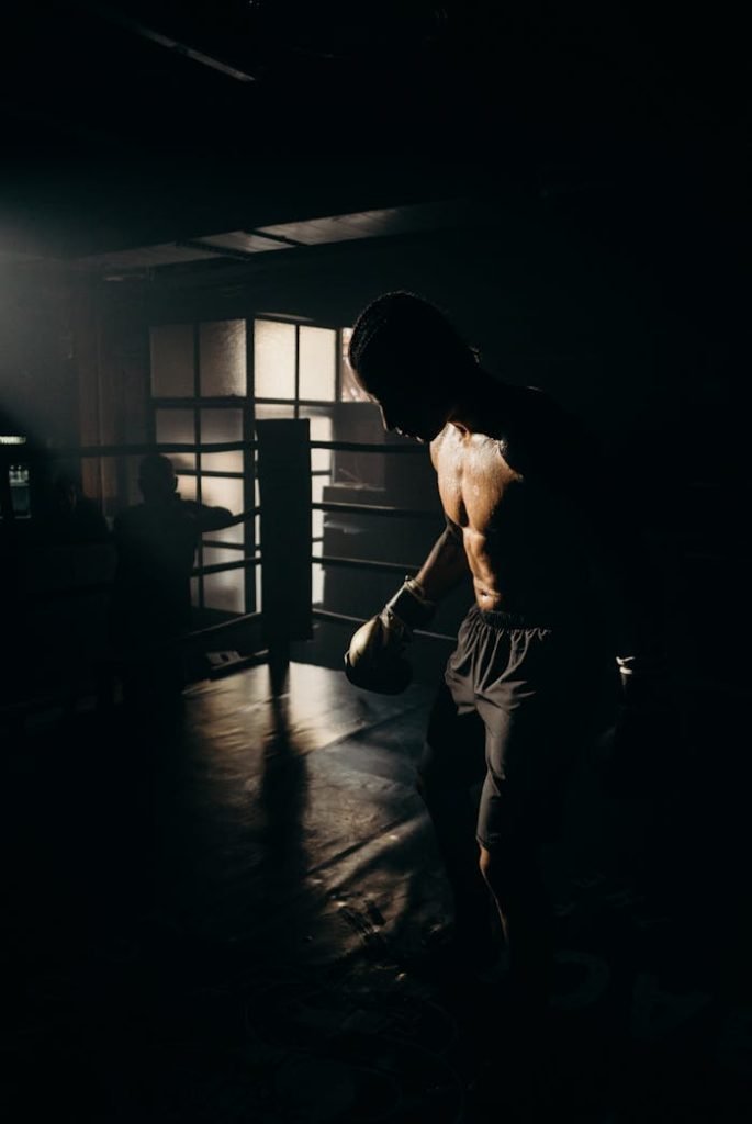 Silhouetted male boxer trains with dramatic lighting, emphasizing strength and focus.