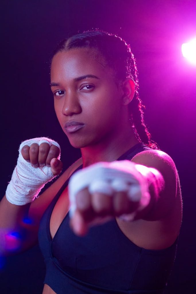 Strong female boxer in sports bra with hand wraps, ready to punch. Vibrant lighting.